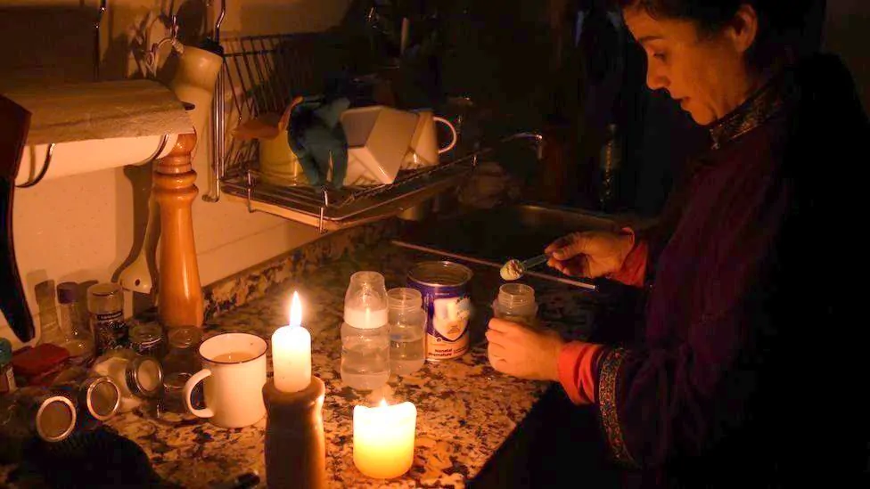 Donna intenta ad accendere candele sul bancone della cucina per non accendere la luce